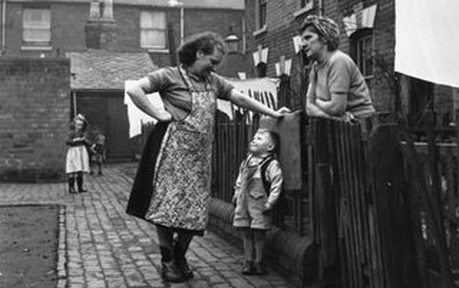 Two ladies learning on garden fence with little boy looking up at them in alley between their houses. Neighbours talking over the garden fence in the 1950's . Neighbours can often help trace the history of a house